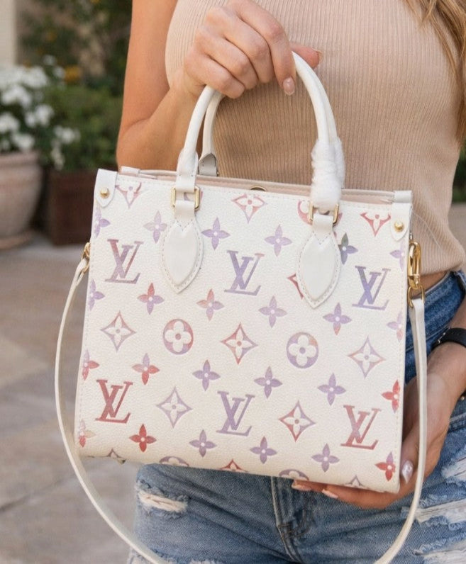 A person holding a white Louis Vuitton monogram handbag with gold-tone hardware and white leather handles, wearing a beige ribbed top and distressed blue jeans.